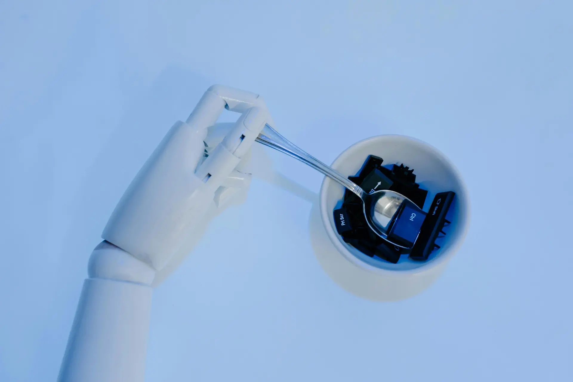 A robotic hand holds a spoon filled with keyboard keys, symbolizing AI and technology fusion.